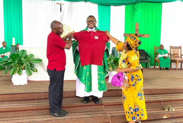 Paroko wa Parokia ya Familia Takatifu – Mburahati, Jimbo Kuu Katoliki la Dar es Salaam, Padri Vitalis Kassembo, akipokea zawadi ya ‘T-shirt’ kutoka wawakilishi wa Tumaini Media wakati wa Adhimisho la Misa Takatifu ya Shukrani kwa kutimiza Miaka 30 ya Redio Tumaini, iliyoadhimishwa parokiani hapo. (Picha na Mathayo Kijazi)